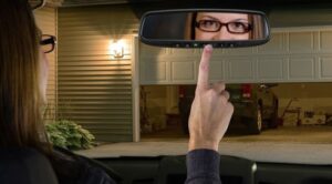 a woman opening her garage door by pressing a button on her car's rearview mirror